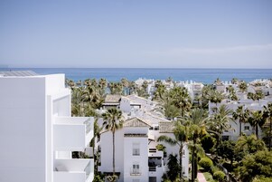 A coastal residential area with white buildings, palm trees, and a view of the sea.