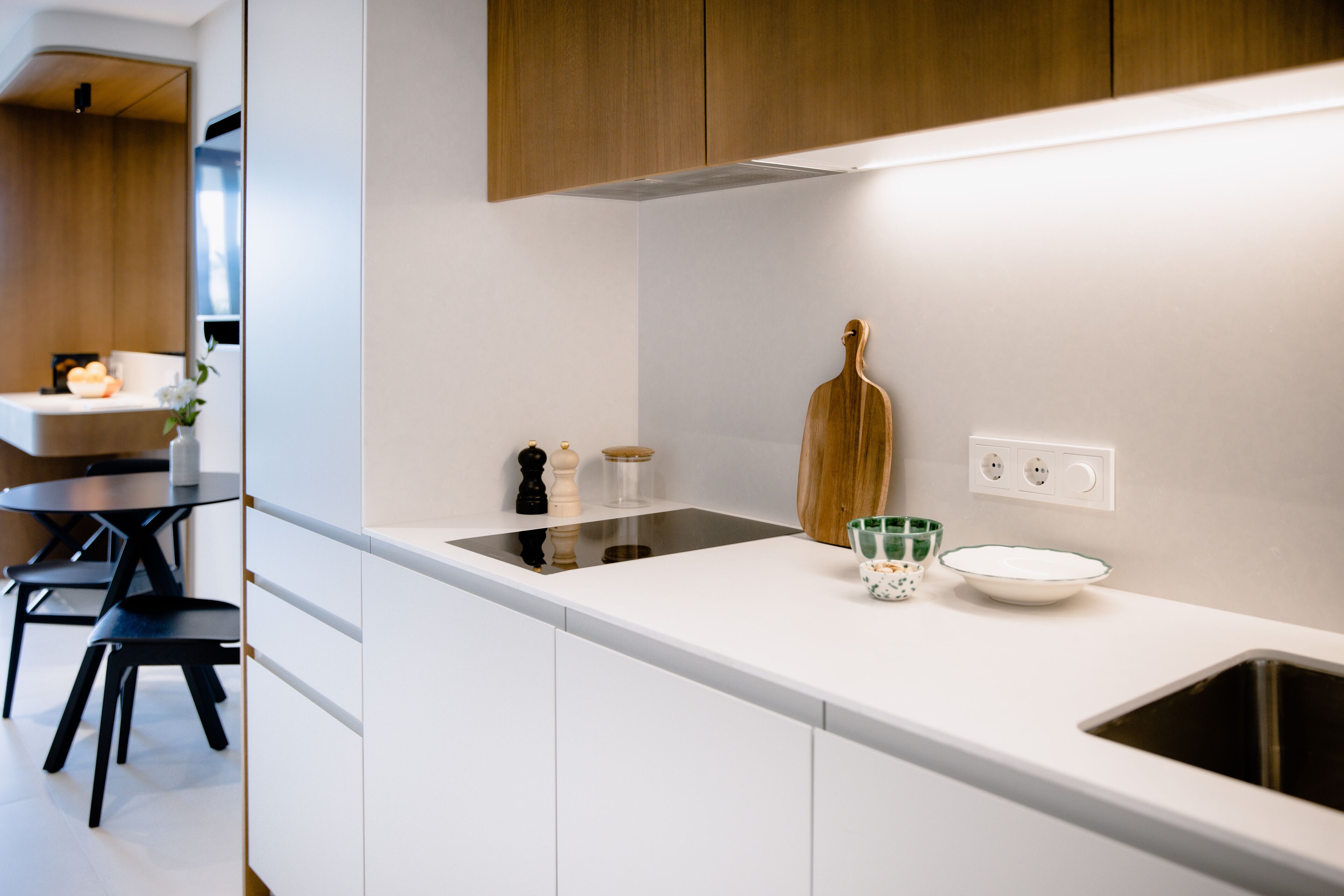 A modern kitchen with white cabinetry, a black countertop, and a wooden cutting board.