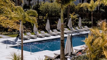 Una piscina al aire libre, sombrillas, sillones reclinables de piscina