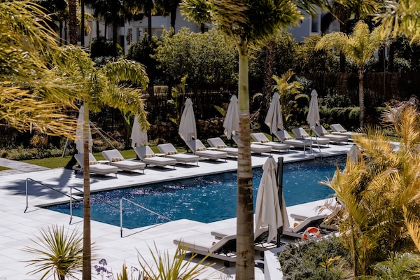 Una piscina al aire libre, sombrillas, sillones reclinables de piscina