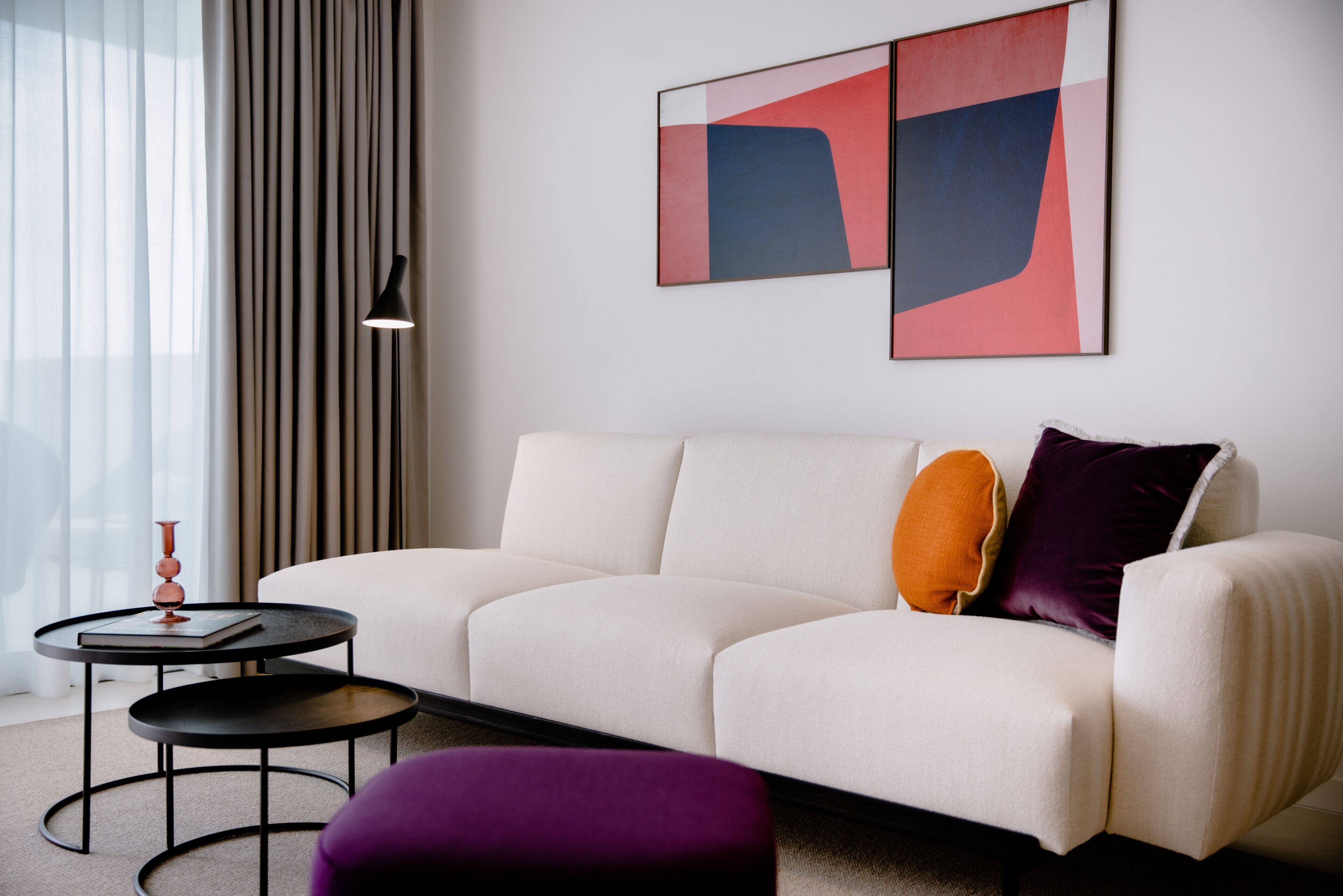 Un salon moderne avec un canapé blanc, une table basse ronde et une table d’appoint sur laquelle se trouvent un livre et un vase.