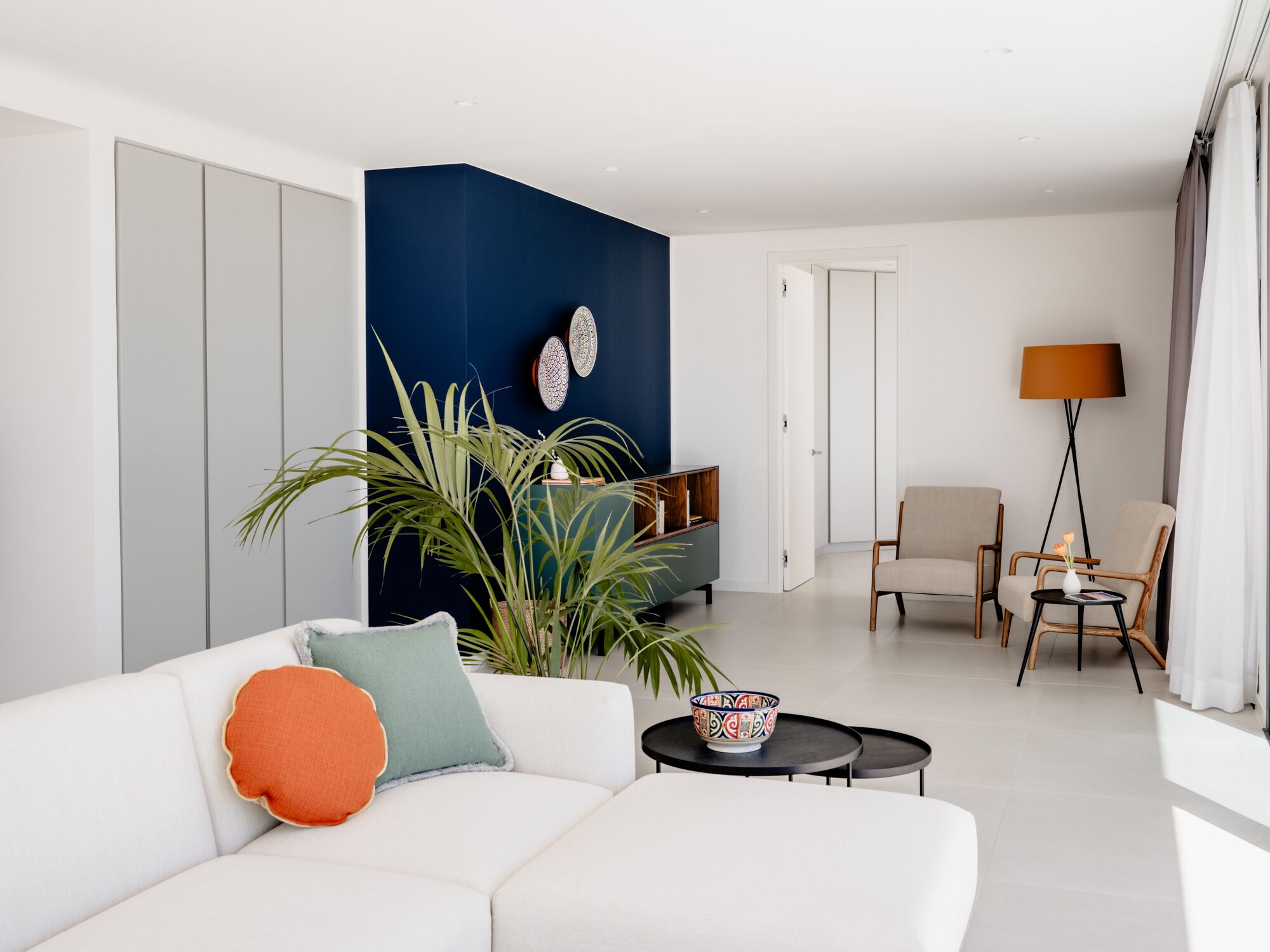 Una sala de estar moderna con un sofá blanco, una mesa de centro, una lámpara de pie, una mesita auxiliar y una estantería.