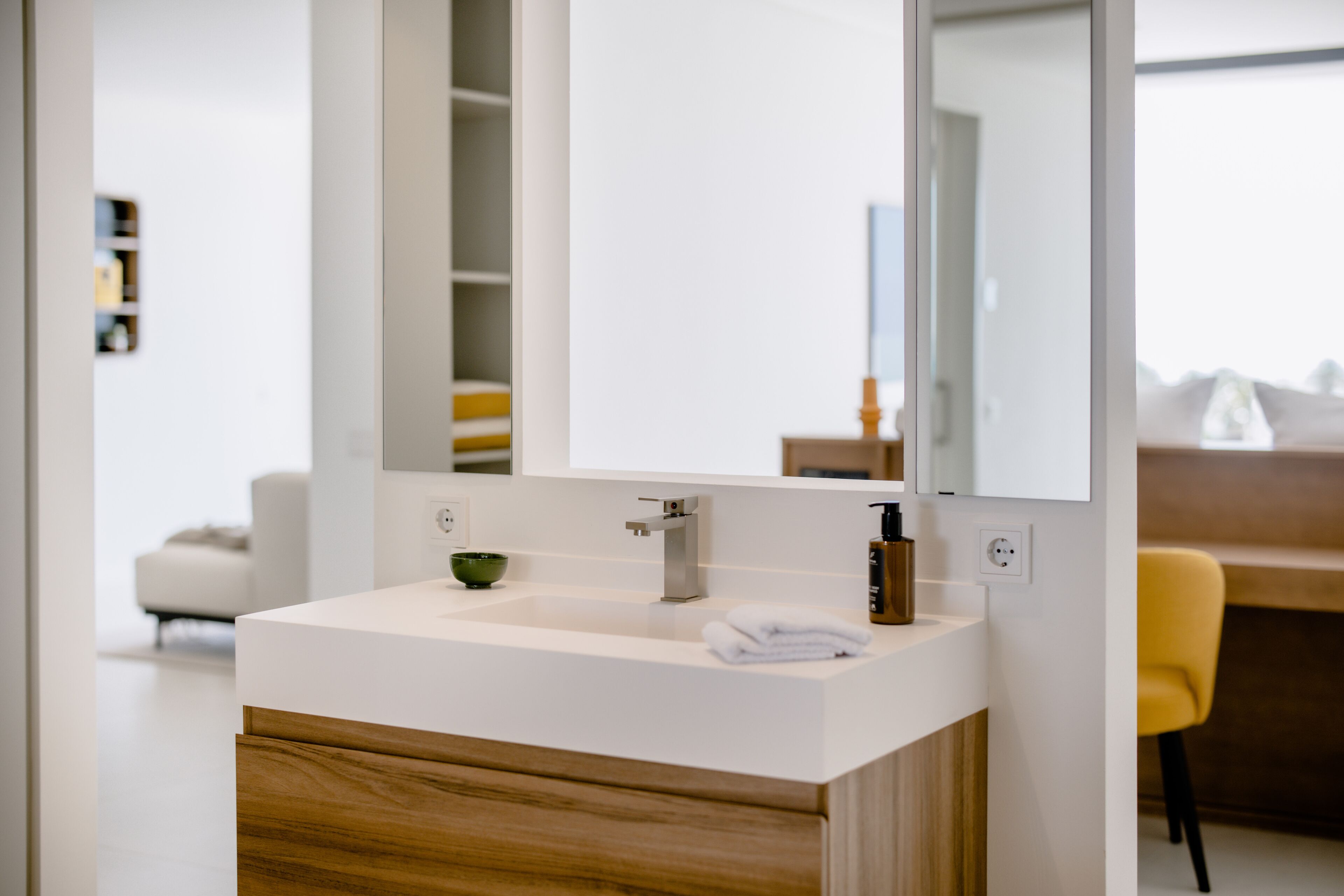 A modern bathroom with a white sink, wooden cabinet, and a large mirror.