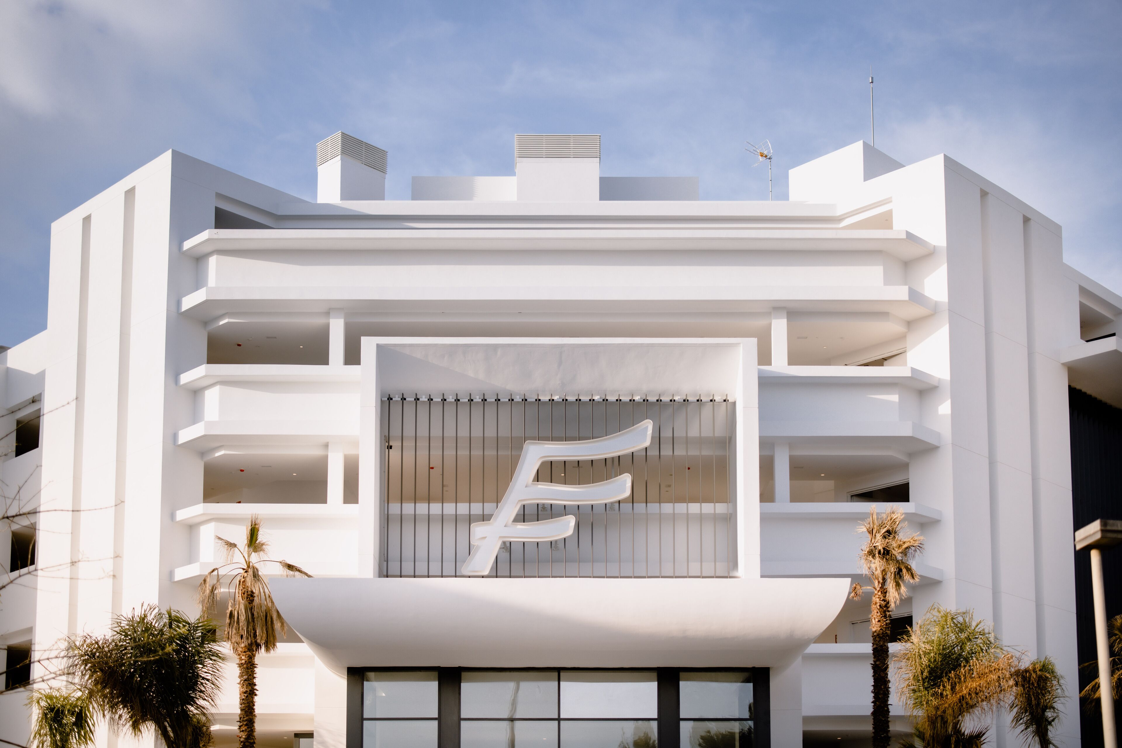 A modern building with a prominent 'E' logo, multiple balconies, and palm trees.