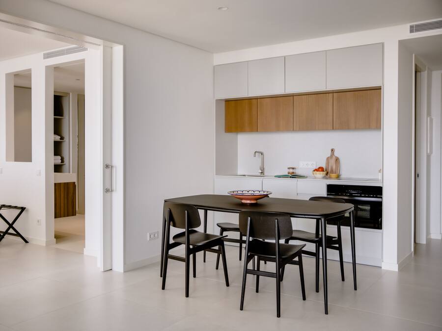 Una cocina moderna con armarios blancos, encimera de madera y un comedor con mesa y sillas.