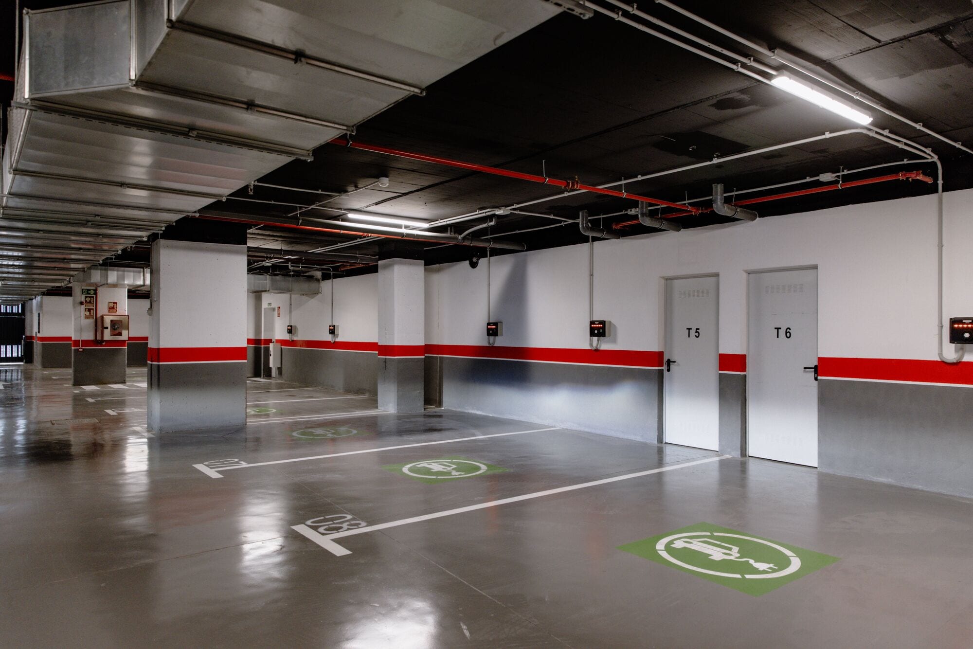 A clean, well-lit parking garage with white walls, red accents, and clear directional markings on the floor.