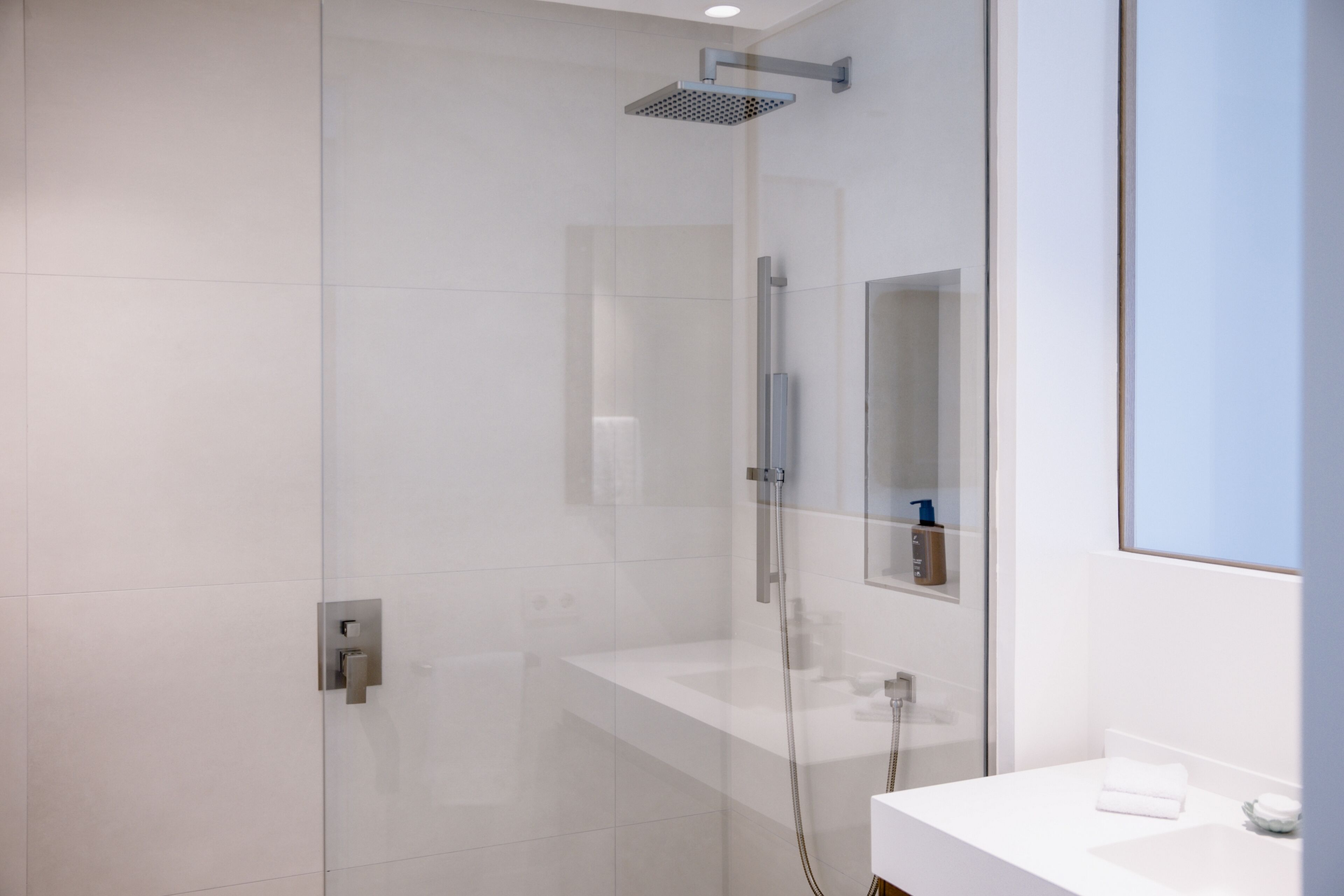 A modern bathroom with a glass-enclosed shower, a white sink, and a mirror above the sink.