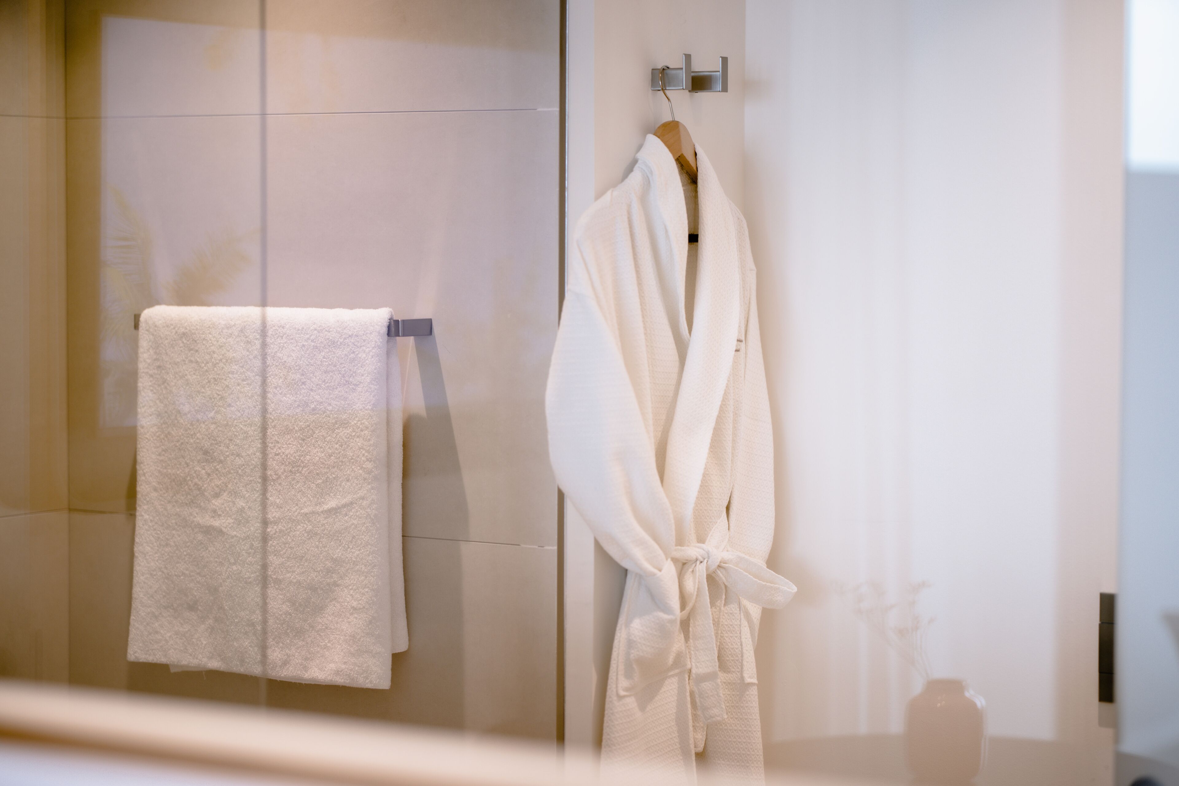 A bathroom with a glass shower door, a white towel, and a white bathrobe hanging on a hook.