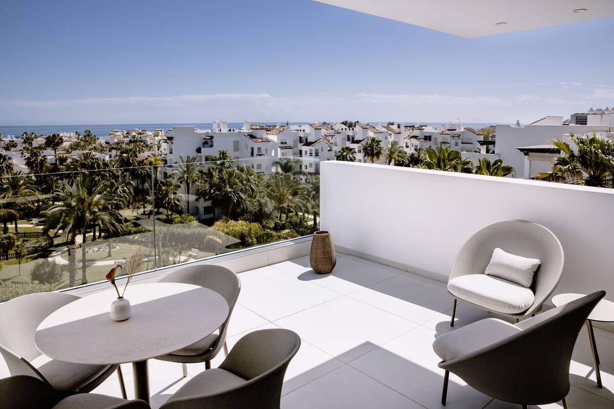 A modern balcony with a white table, two chairs, and a vase.