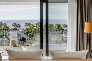A hotel room with a large balcony, a view of the sea, and palm trees.