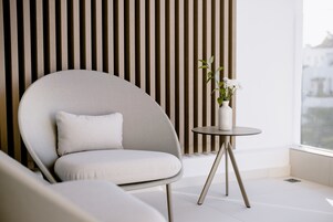Una habitación moderna con un sofá curvo, una mesita redonda con un florero y una pared de listones de madera verticales.