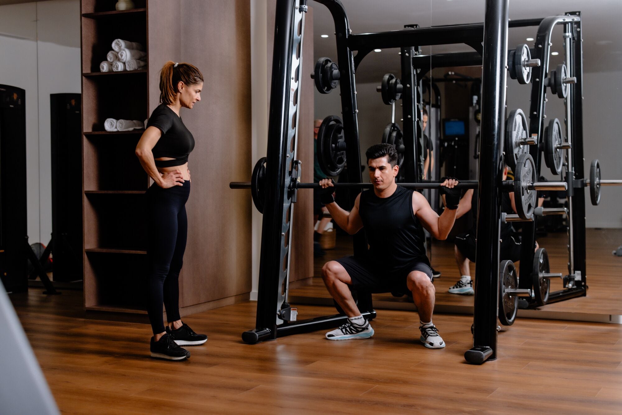 Ein Fitnessstudio mit einem Squat-Stand und einer Frau daneben.