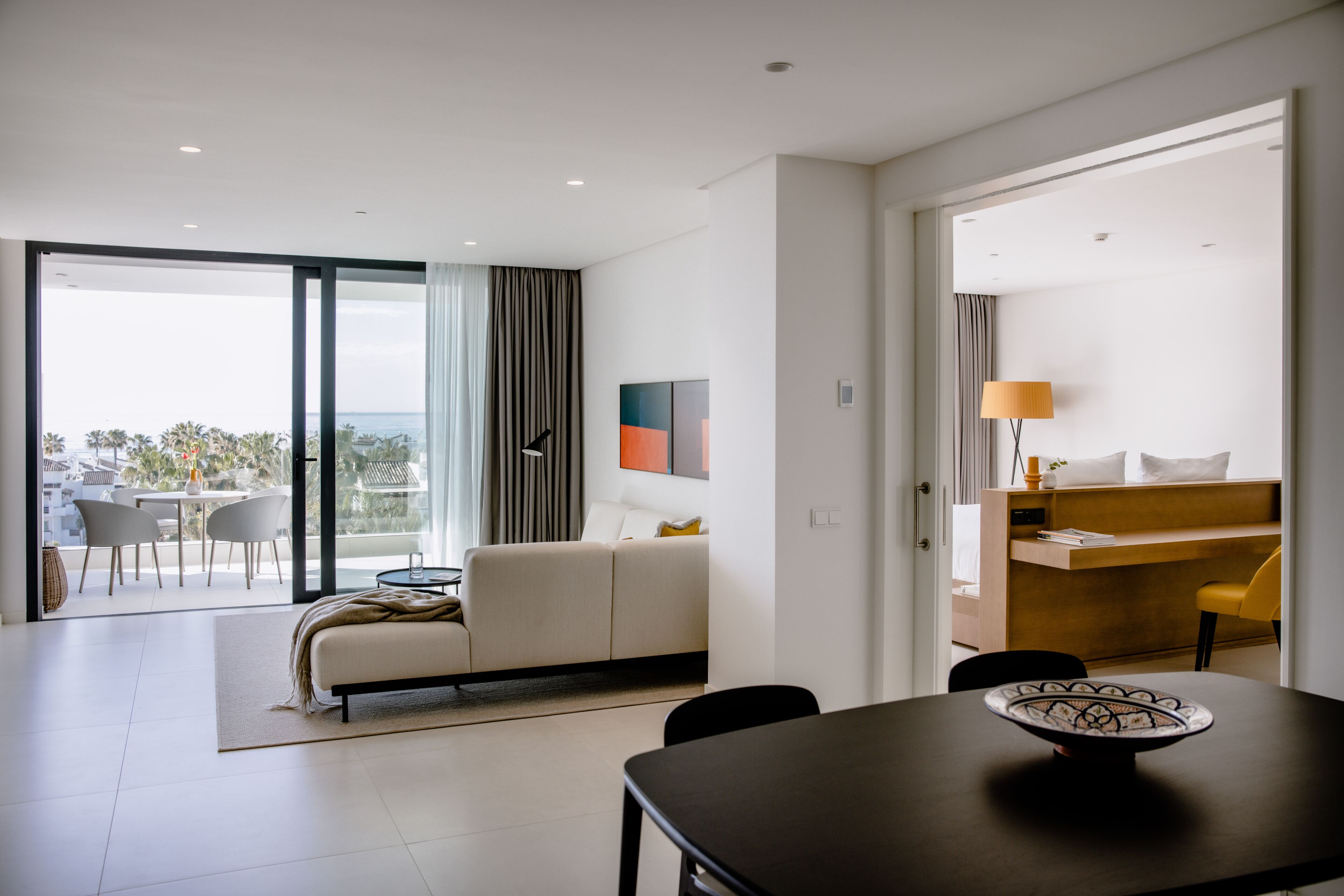 Une chambre d’hôtel moderne dotée d’un balcon, d’un canapé, d’une table à manger et d’un espace bureau.