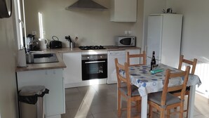 Une cuisine compacte équipée d’un four à micro-ondes, d’une cuisinière, d’un four et d’un évier. Une table à manger avec des chaises est placée près de la fenêtre.