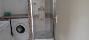 Zona de lavandería con lavadora, cabina de ducha de vidrio y un banco.