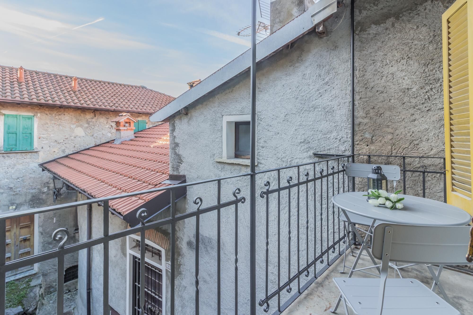 A balcony with a table and chairs, a railing, and a view of neighboring buildings.