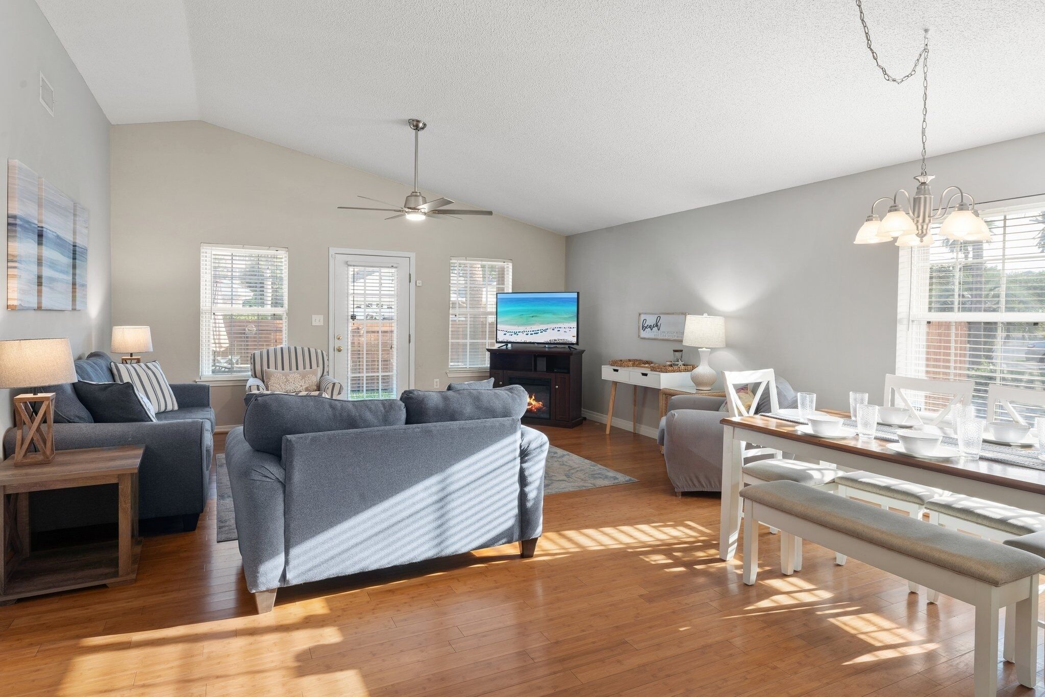 A spacious living room with a grey sofa set, wooden flooring, and a dining area with a bench.