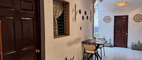 Una habitación con puerta de madera, ventana con cortinas, una mesa con sillas y una lámpara colgante.