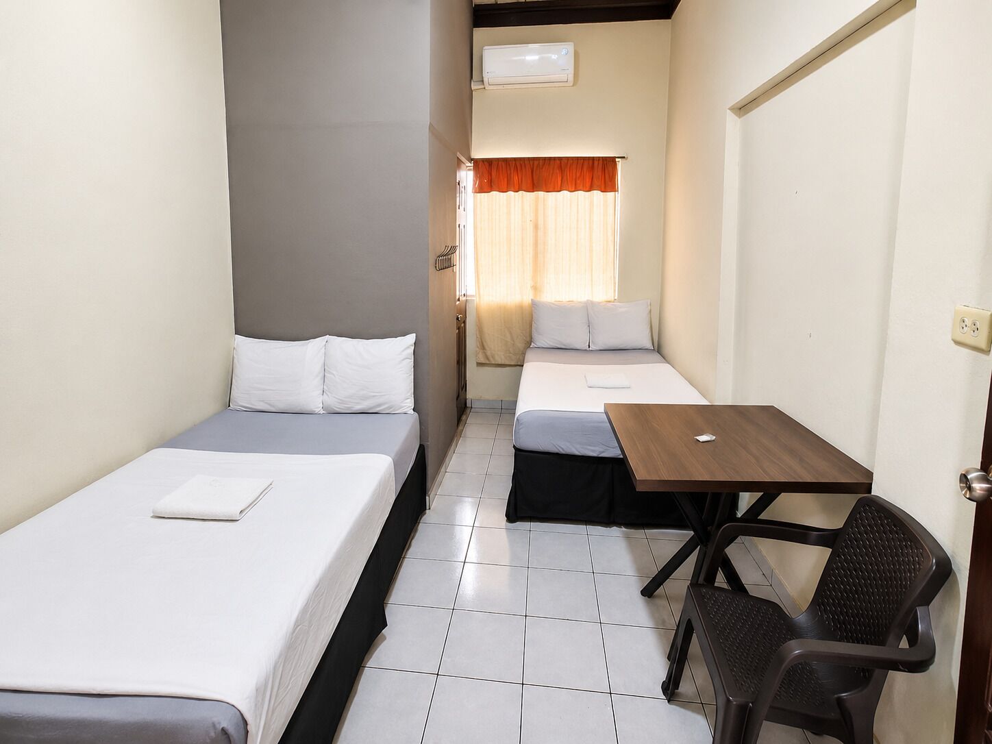 A hotel room with two beds, a small table, and a chair.