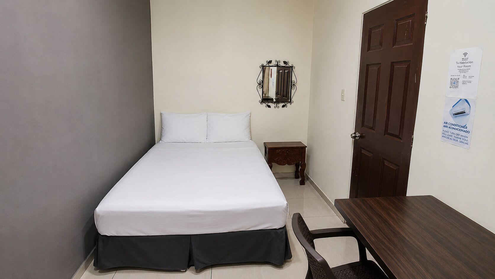 A small, neatly arranged bedroom with a bed, bedside table, and a door.