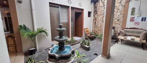 A courtyard with a fountain, potted plants, a sofa, and a stone wall.