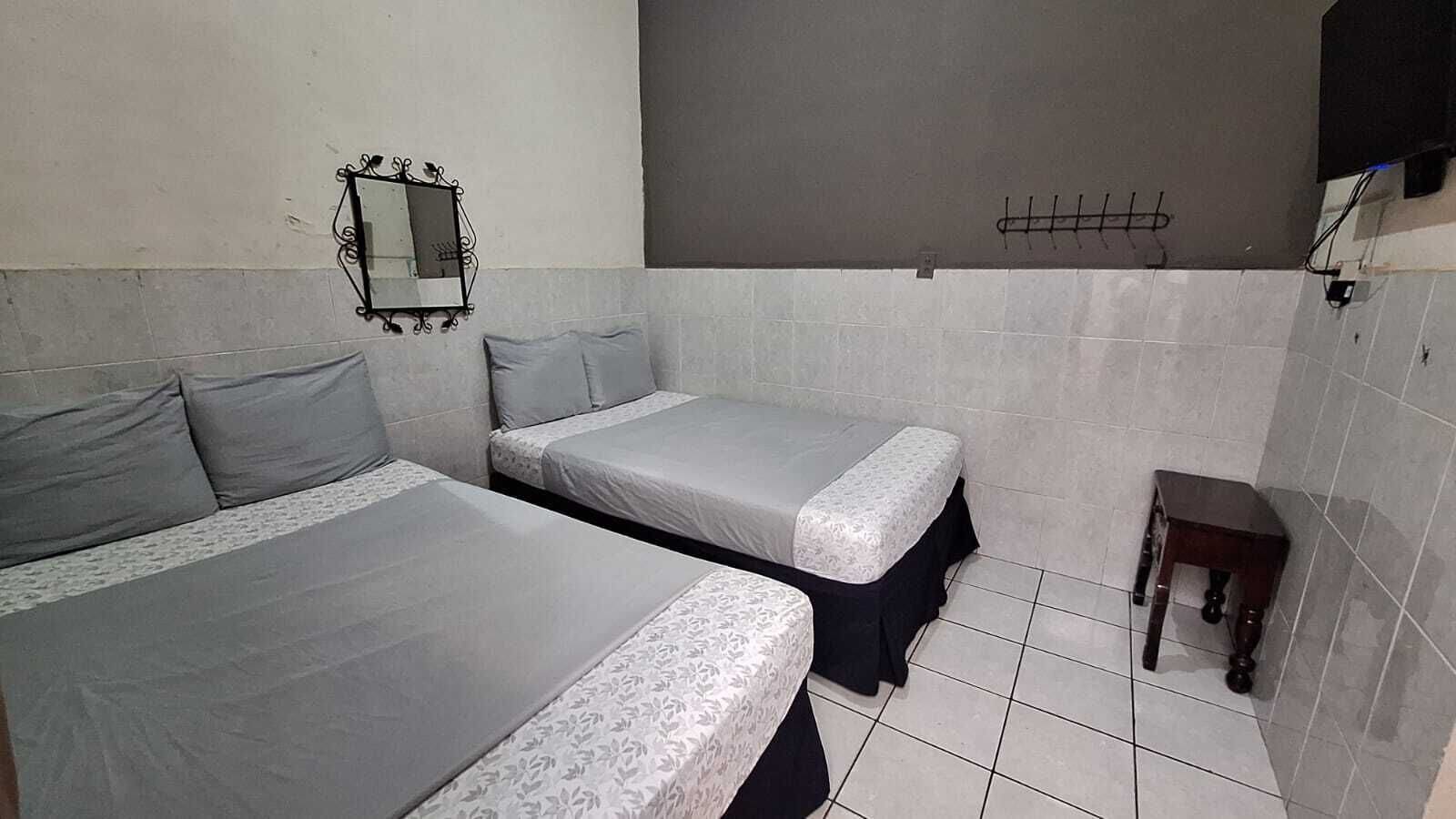 Una habitación pequeña y limpia, con dos camas, un espejo, una mesita y paredes de azulejos.