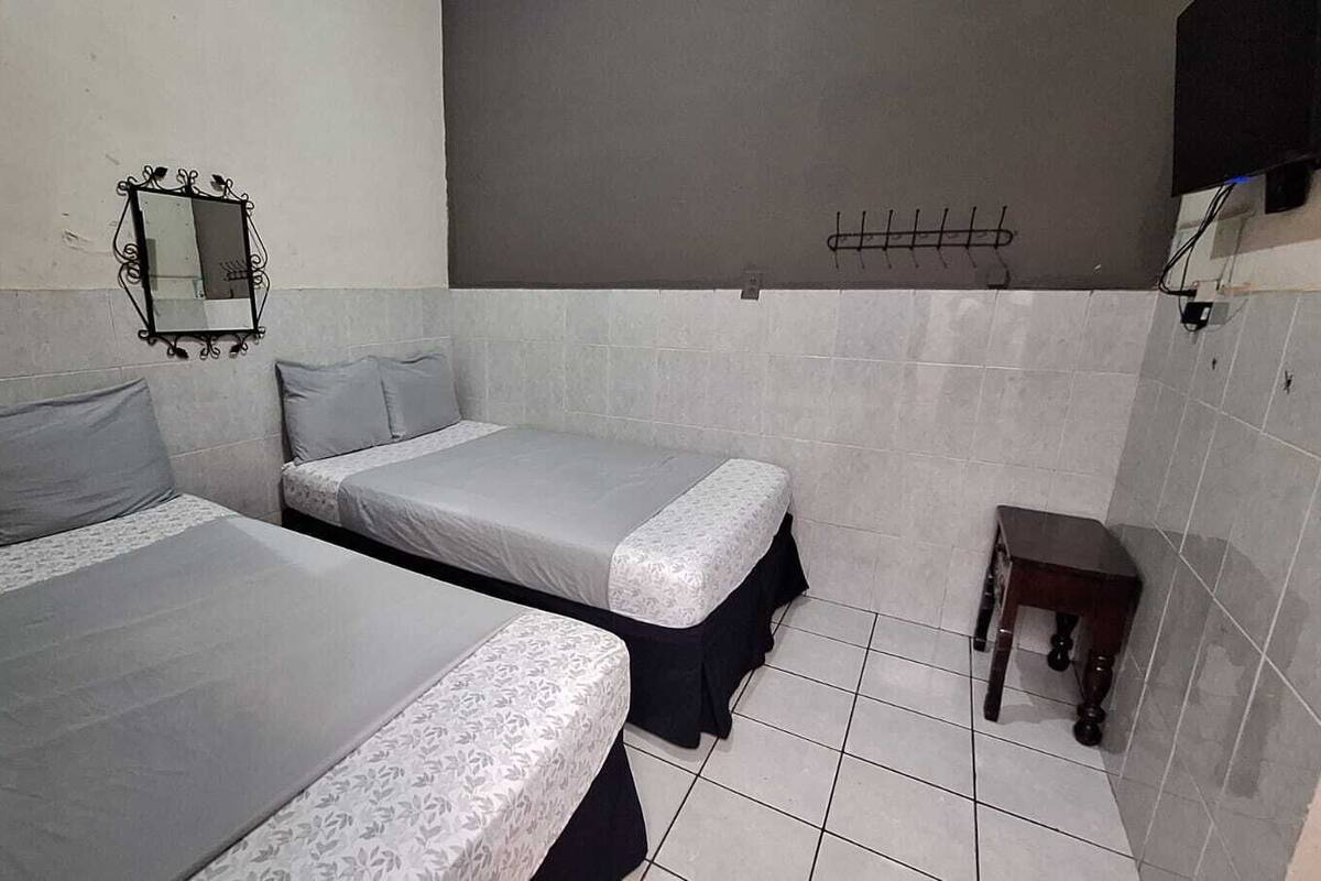A small, clean room with two beds, a mirror, a small table, and tiled walls.