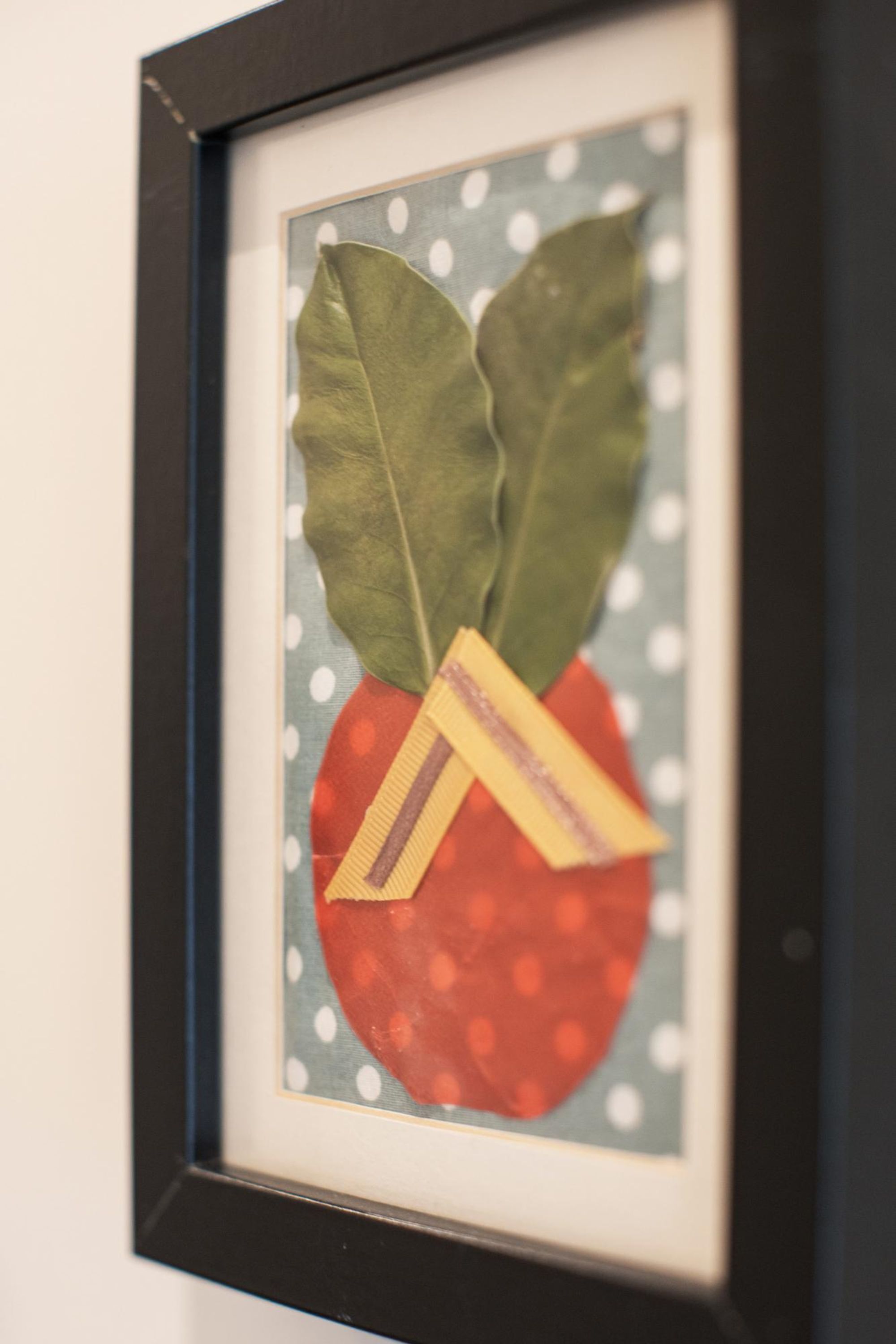A framed artwork of a strawberry with leaves and a tag.