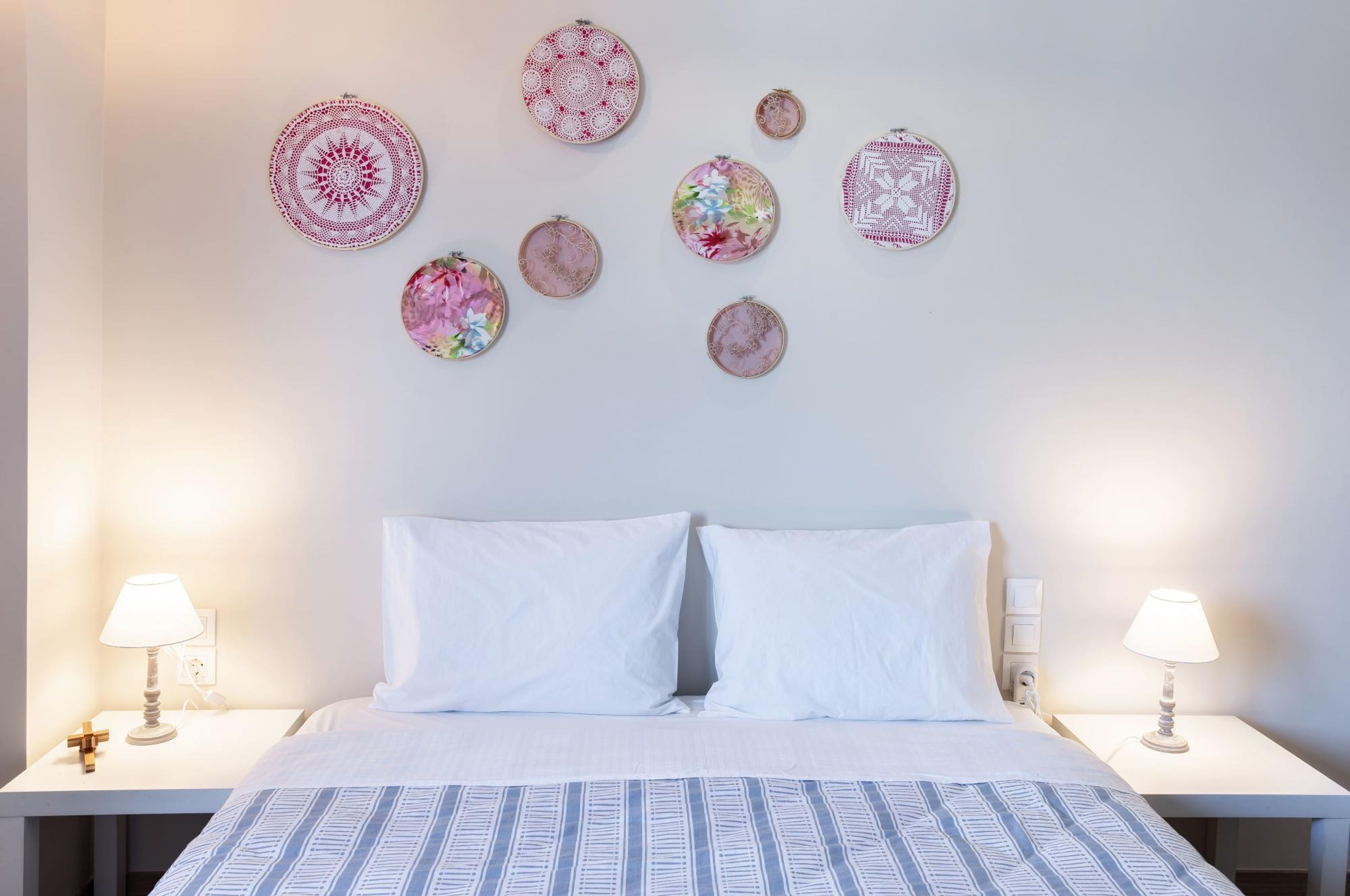 Una cama bien hecha con sábanas blancas y una colcha de cuadros azules, flanqueada por dos mesitas de noche con lámparas, y una pared decorada con objetos circulares.