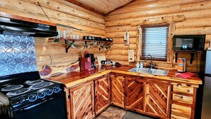 A wooden cabin interior with a kitchen featuring a stove, refrigerator, and wooden cabinets. - Music Mountain Retreat Cabin B (Hot Springs)