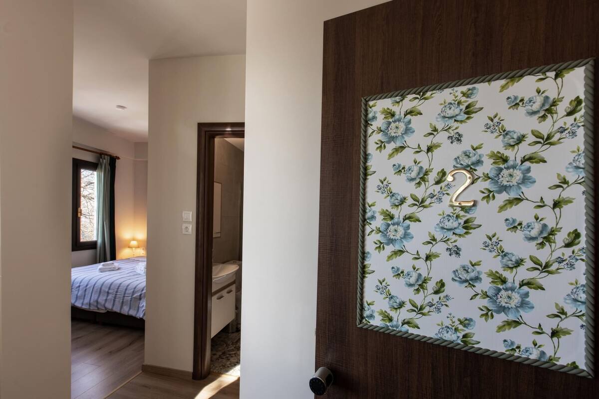 A hotel room with a wooden door, a bed with a striped bedspread, a bedside lamp, and a window with curtains.