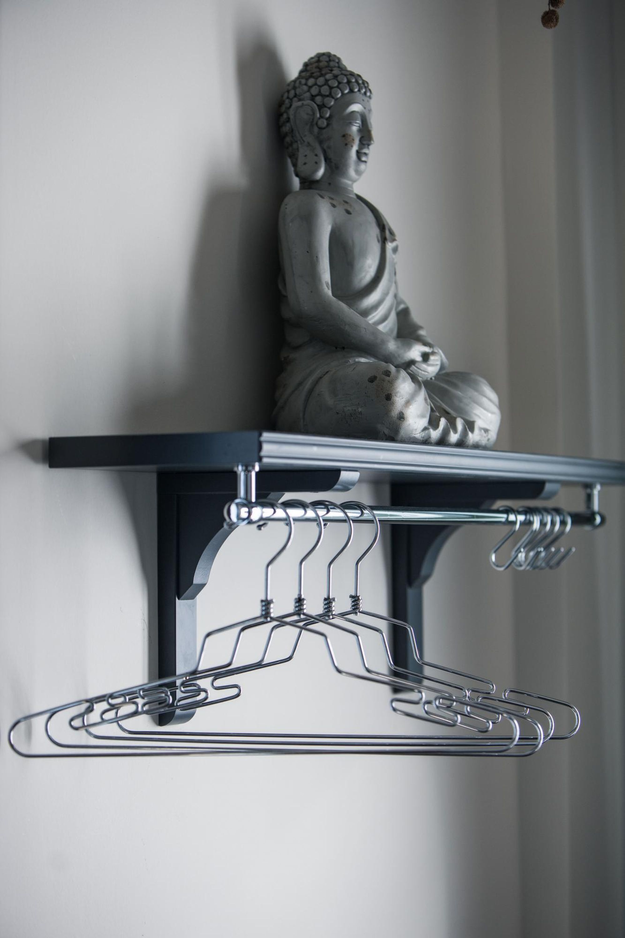 A statue of Buddha on a shelf above a metal hanger rack.