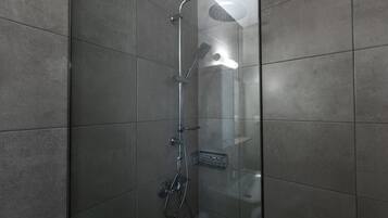A glass-enclosed shower stall with a handheld showerhead, a wall-mounted faucet, and a handheld showerhead.