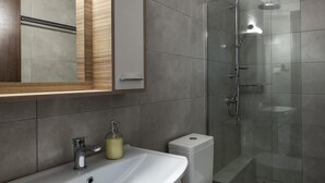 A modern bathroom with a white sink, mirror, and toilet. It features a shower with a glass door and a patterned floor. - Stagiates Guest House Room 2 (Volos)