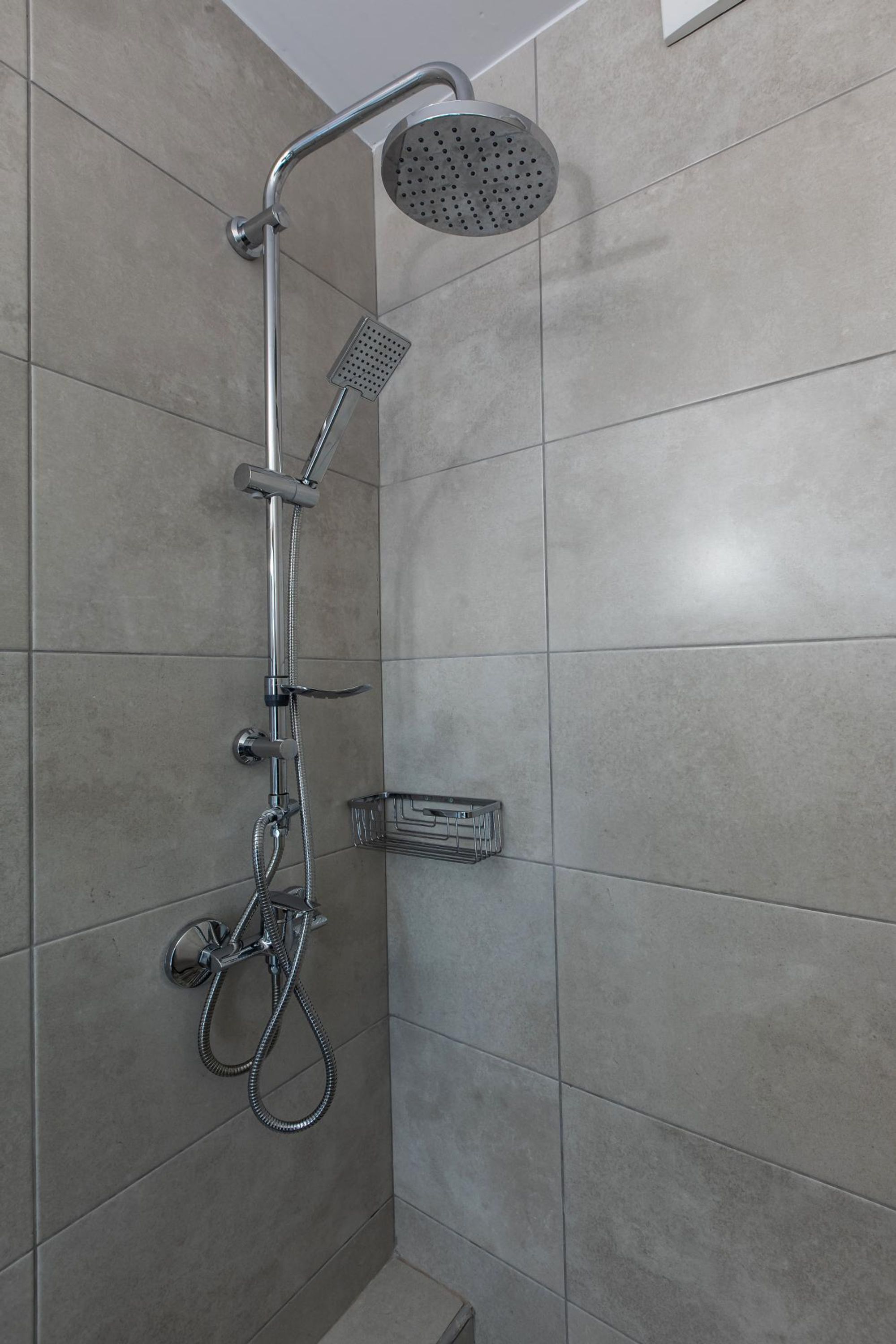 A shower with a handheld showerhead and a wall-mounted faucet.