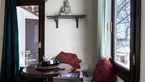 A cozy room with a wooden floor, a round table with a tray, a bench with a blanket, and a window with a view of trees. - Stagiates Guest House Room 2 (Volos)