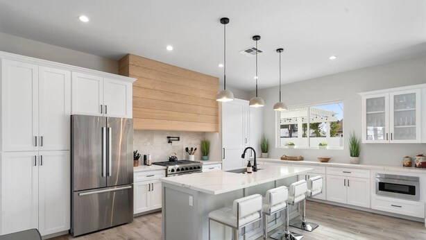 A modern kitchen with white cabinetry, stainless steel appliances, a central island with bar stools, pendant lighting, and a view of the outdoors through a window. - Desert Escape | Poolside BBQs, Sunset Views & Spacious Comfort (Phoenix)
