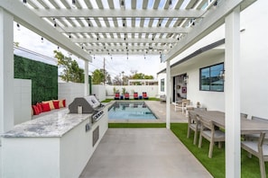 A covered outdoor area with a pool, a barbecue grill, and seating arrangements. - Desert Escape | Poolside BBQs, Sunset Views & Spacious Comfort (Phoenix)