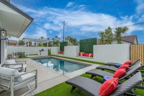 Un espace piscine extérieur moderne, doté de chaises longues, d’un barbecue et d’une pergola.