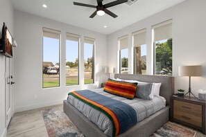 Une chambre à coucher moderne, dotée d’un grand lit, d’un ventilateur de plafond et de plusieurs fenêtres donnant sur l’extérieur.