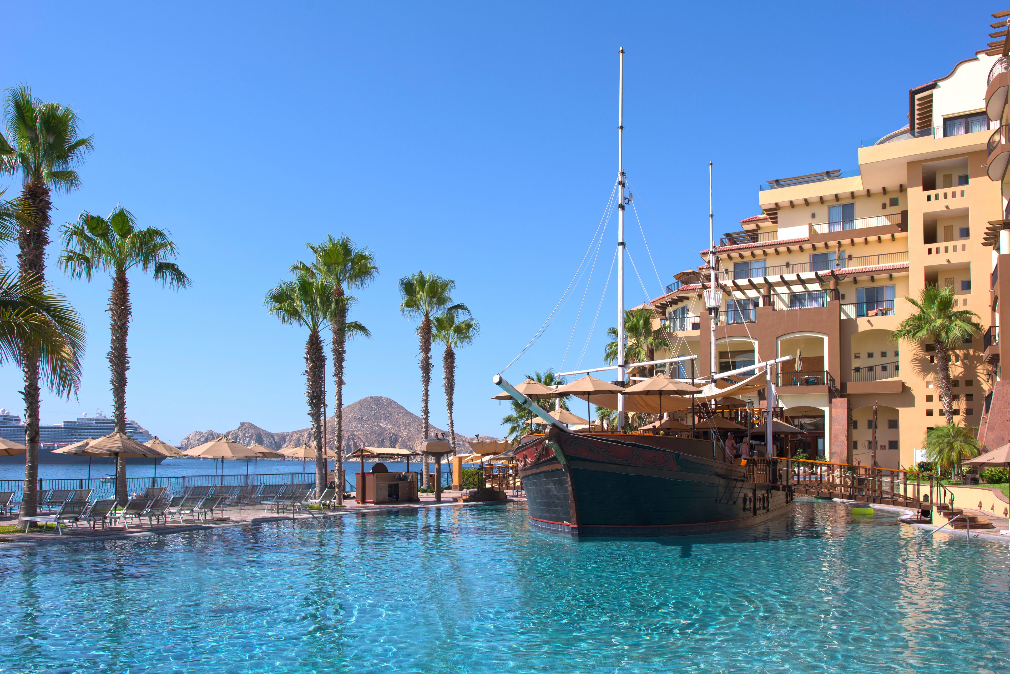 A pool with a boat, palm trees, and a building with balconies.