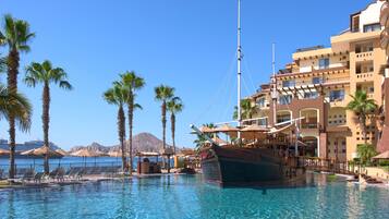 A pool with a boat, palm trees, and a building with balconies.