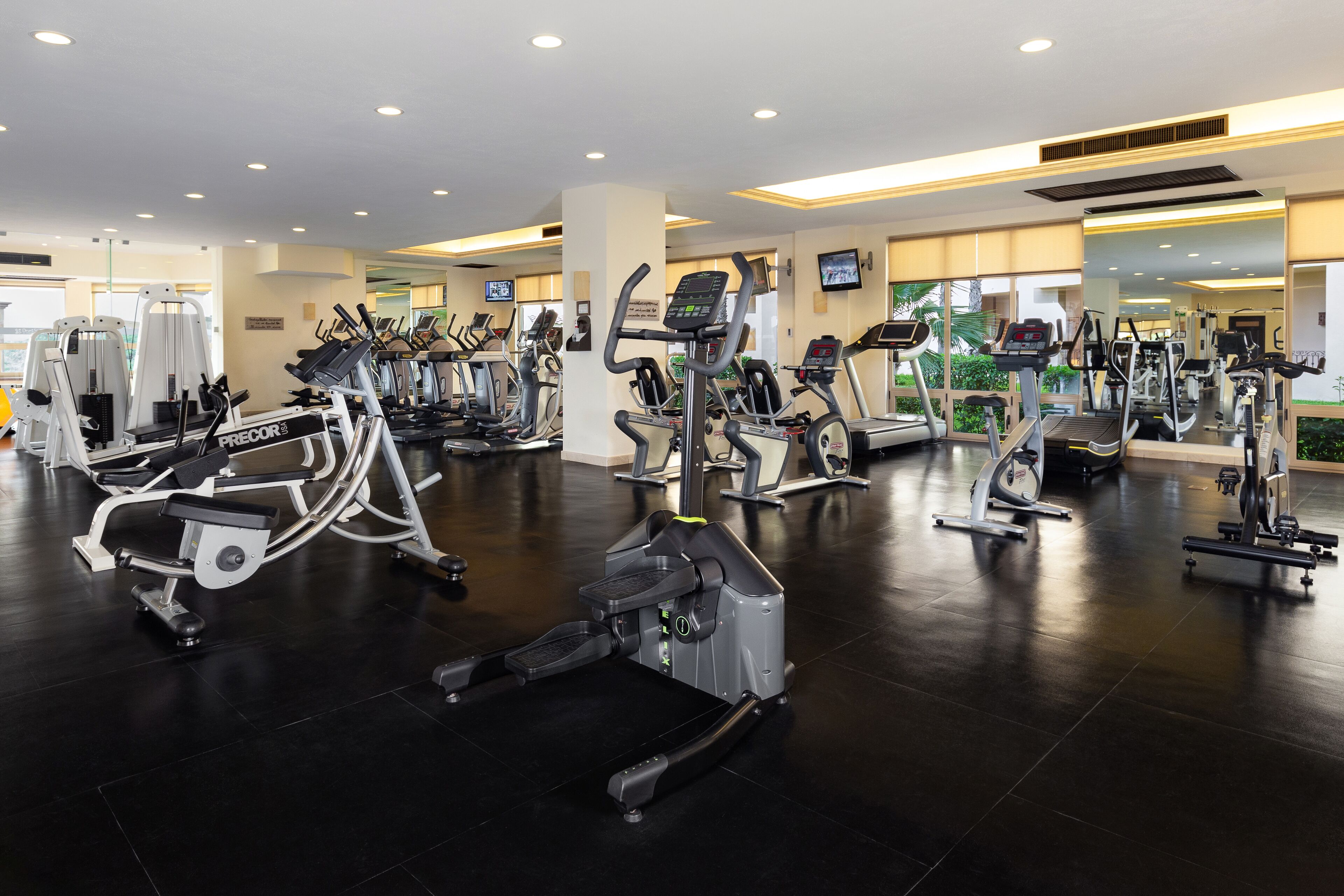 A gym with various cardio machines, including treadmills and elliptical trainers, arranged in rows.