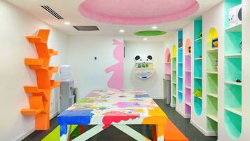 Una habitación de colores vivos con una gran mesa cubierta de pintura, un estante con temática de panda y estanterías coloridas a lo largo de las paredes.