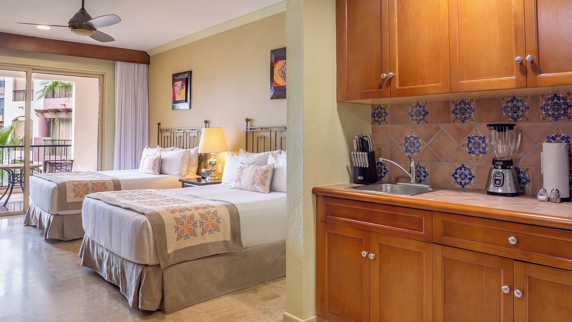 A hotel room with two beds, a kitchenette, and a balcony with a view.