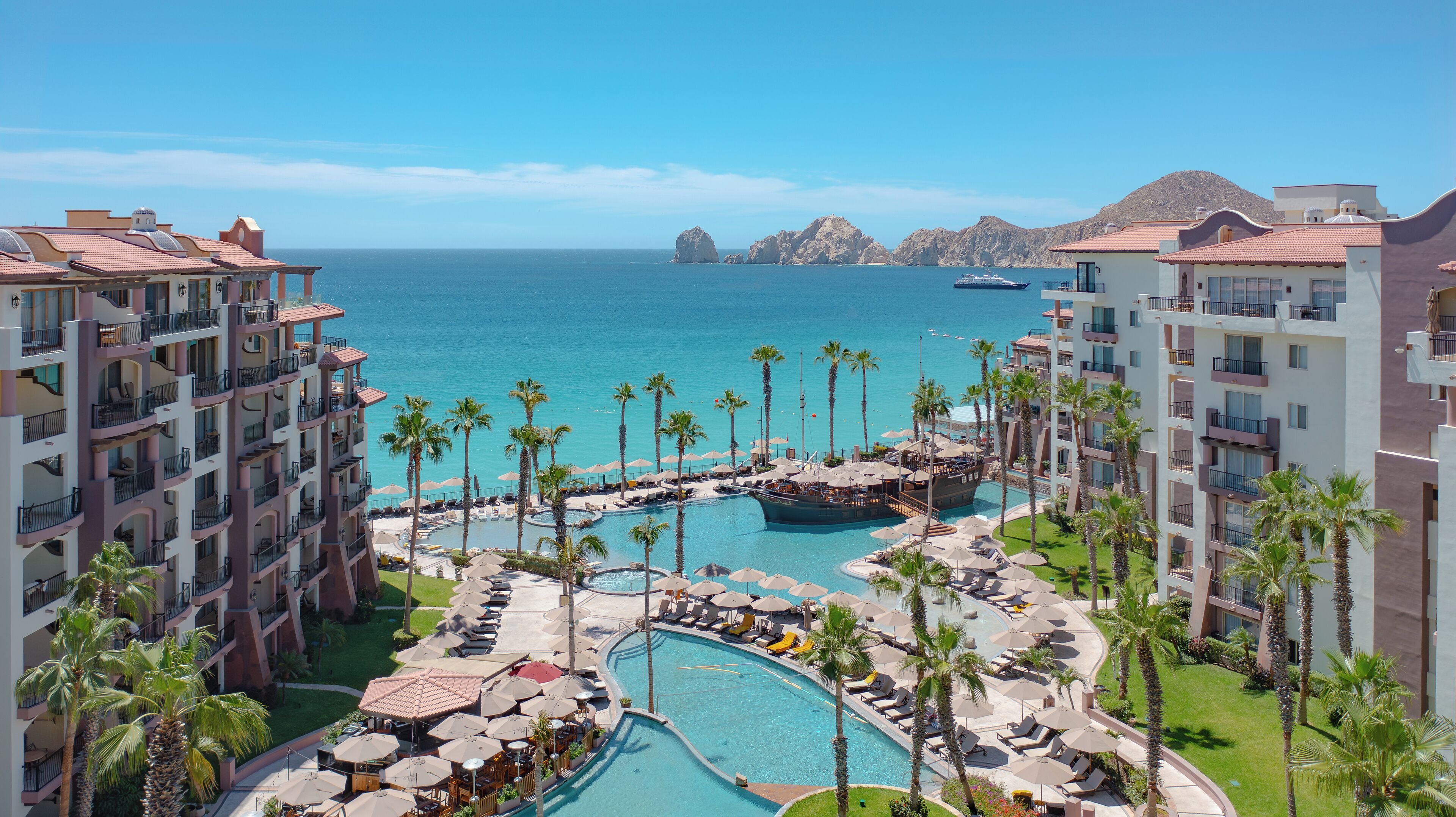 Un resort con varias piscinas, palmeras y vista al océano.
