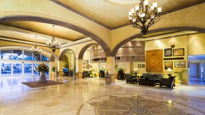 A spacious lobby with high ceilings, arched doorways, and a central chandelier. There are several potted plants and a large, ornate rug on the polished floor. - Villa del Arco Beach Resort & Spa Cabo San Lucas - All Inclusive (Cabo San Lucas)