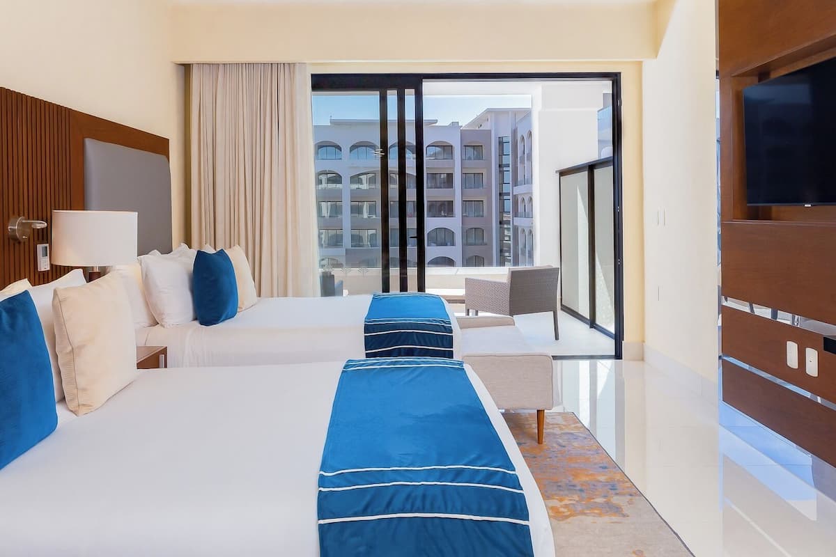 A hotel room with two beds, a TV, a balcony with a view of buildings, and a modern design.