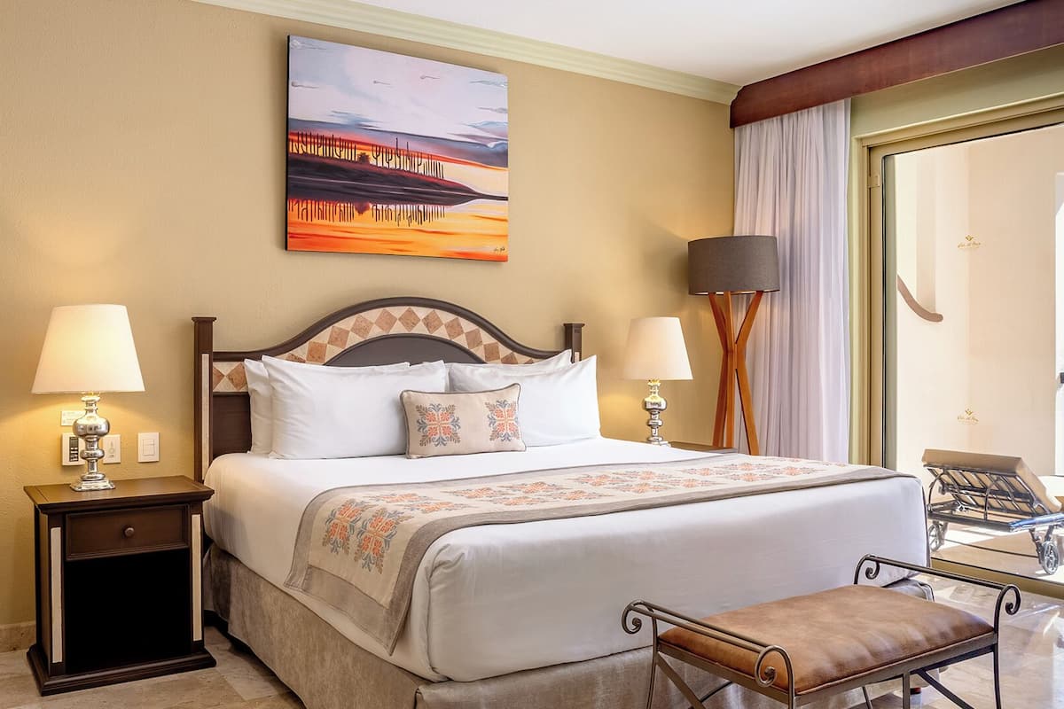 A hotel room with a large bed, two bedside tables with lamps, a chair, and a painting on the wall.