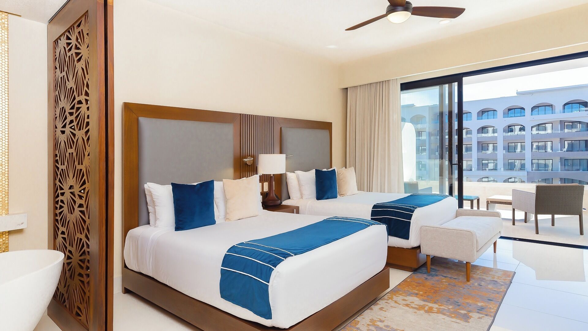 A hotel room with two beds, a balcony, and a view of a building.